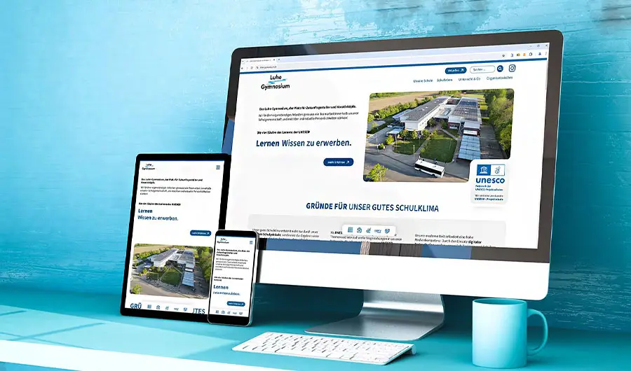 Ein Desktop, ein Tablet und ein Smartphone zeigen dieselbe Schulwebsite - Webdesign aus Harburg - mit einer blauen Tasse neben dem Monitor.