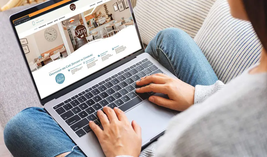 Eine Person sitzt auf einer Couch und surft mit einem Laptop im Webdesign eines Hamburger Cafés.